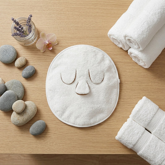 Soma cotton facial hot compress towel laid on a wooden spa table with massage stones, lavender and an orchid